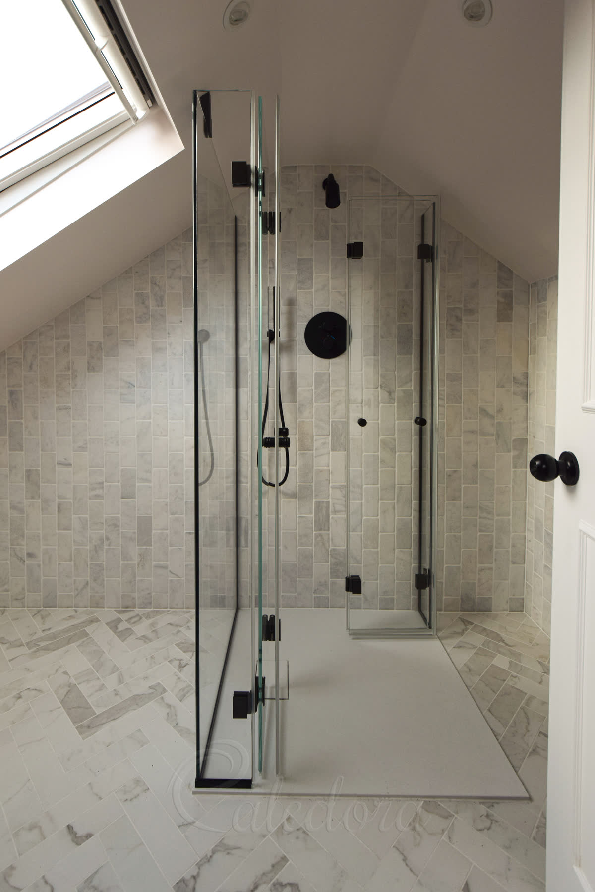 Black bifold shower door installed under eaves with angled ceiling and black hinges