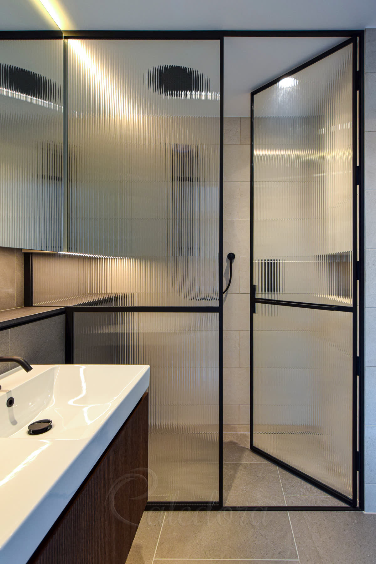 Black shower door partially open showing slim threshold covering tile grout line