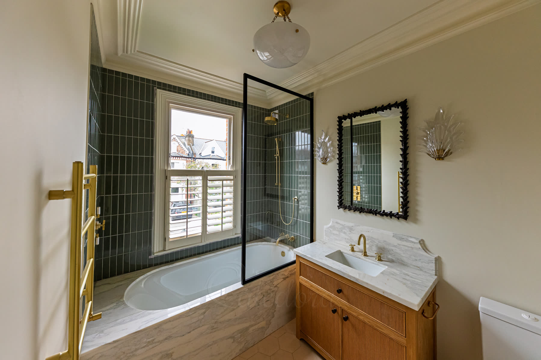 Black shower screen over bath viewed from bathroom showing brass fixtures and wood surround