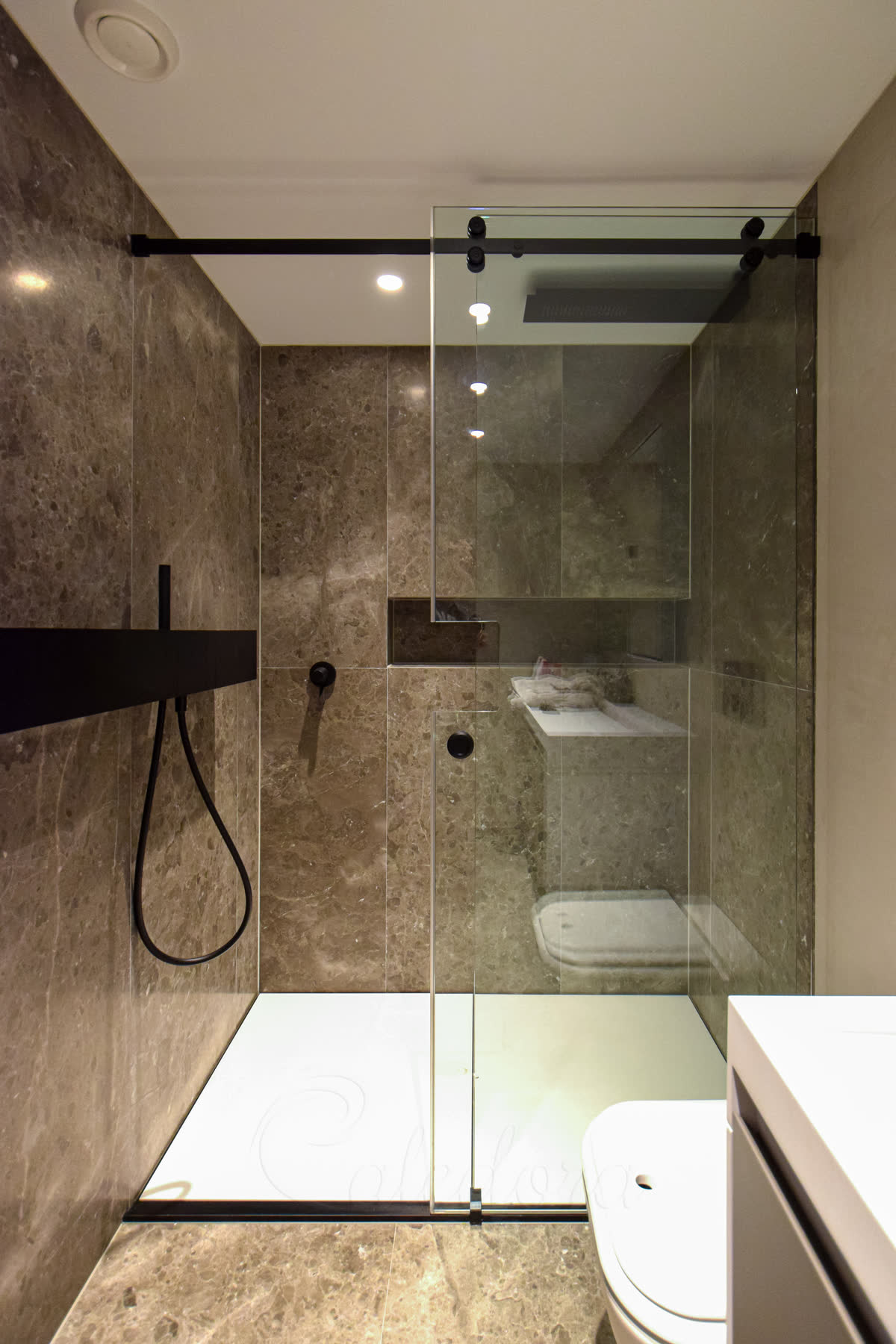 Frameless black sliding shower door with notched glass design for perfect fit around wall-mounted shelf