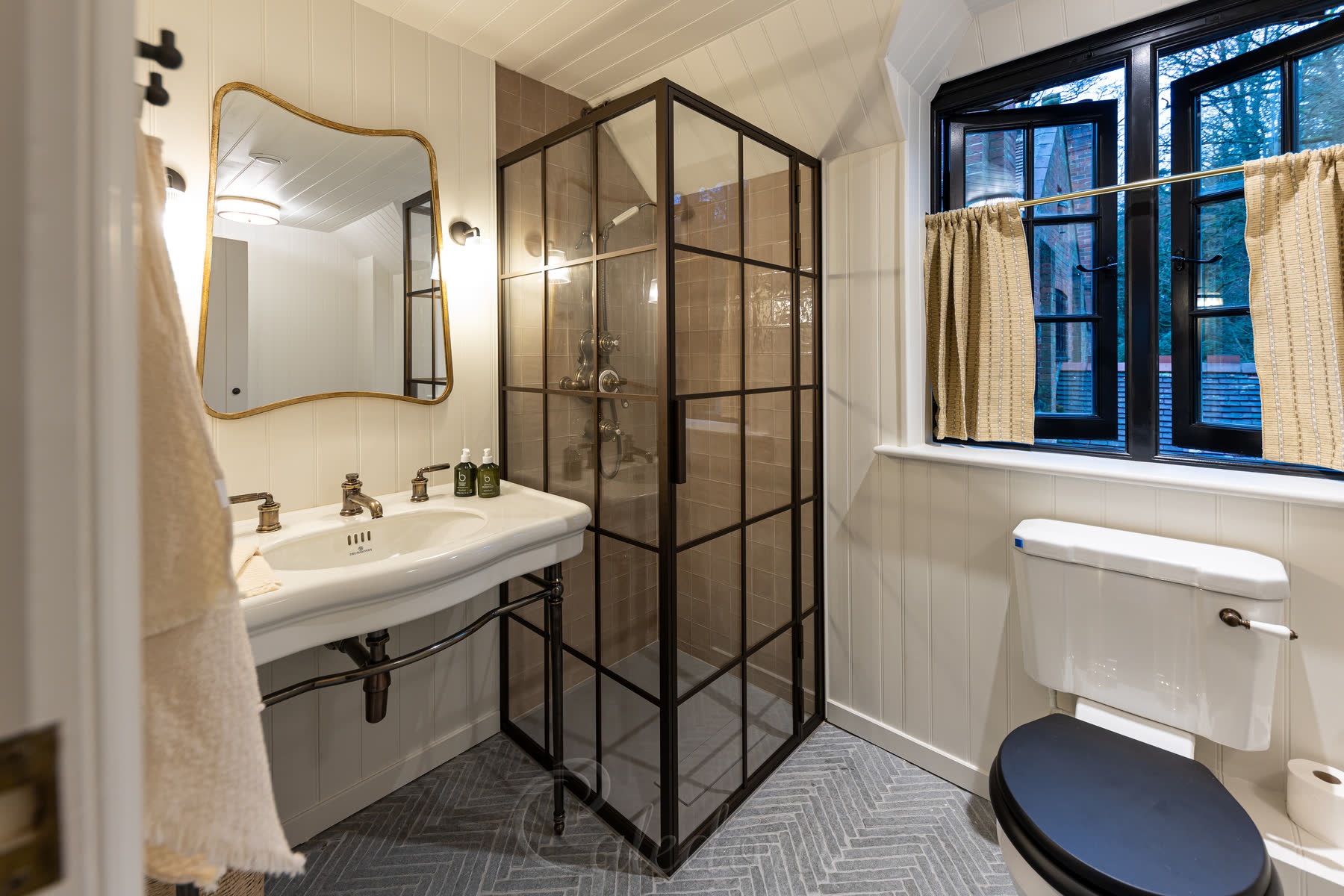 Full view of the bronze grid shower enclosure showing the stone floor and tiled walls