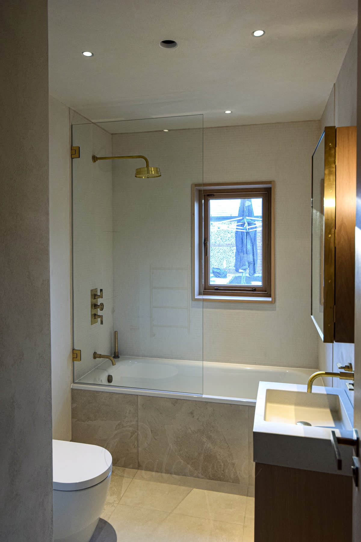 another view of first bathroom with brushed gold shower screen over bath closed