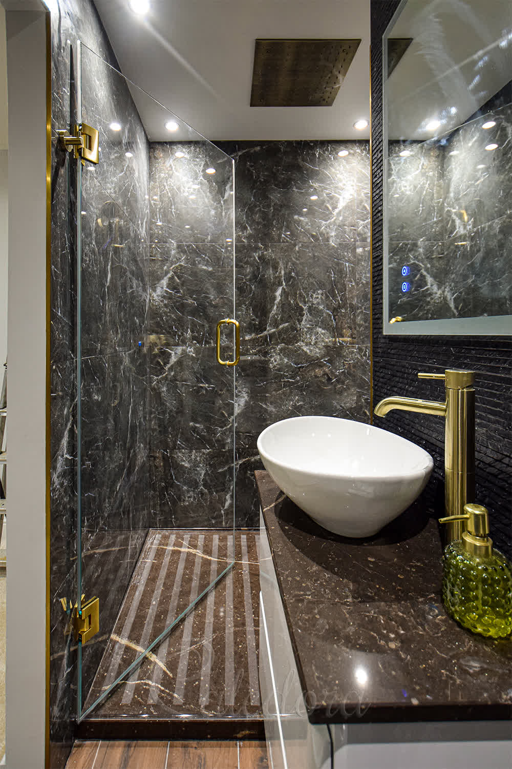 Brushed brass shower door with handle and hinges in contemporary bathroom with black stone walls