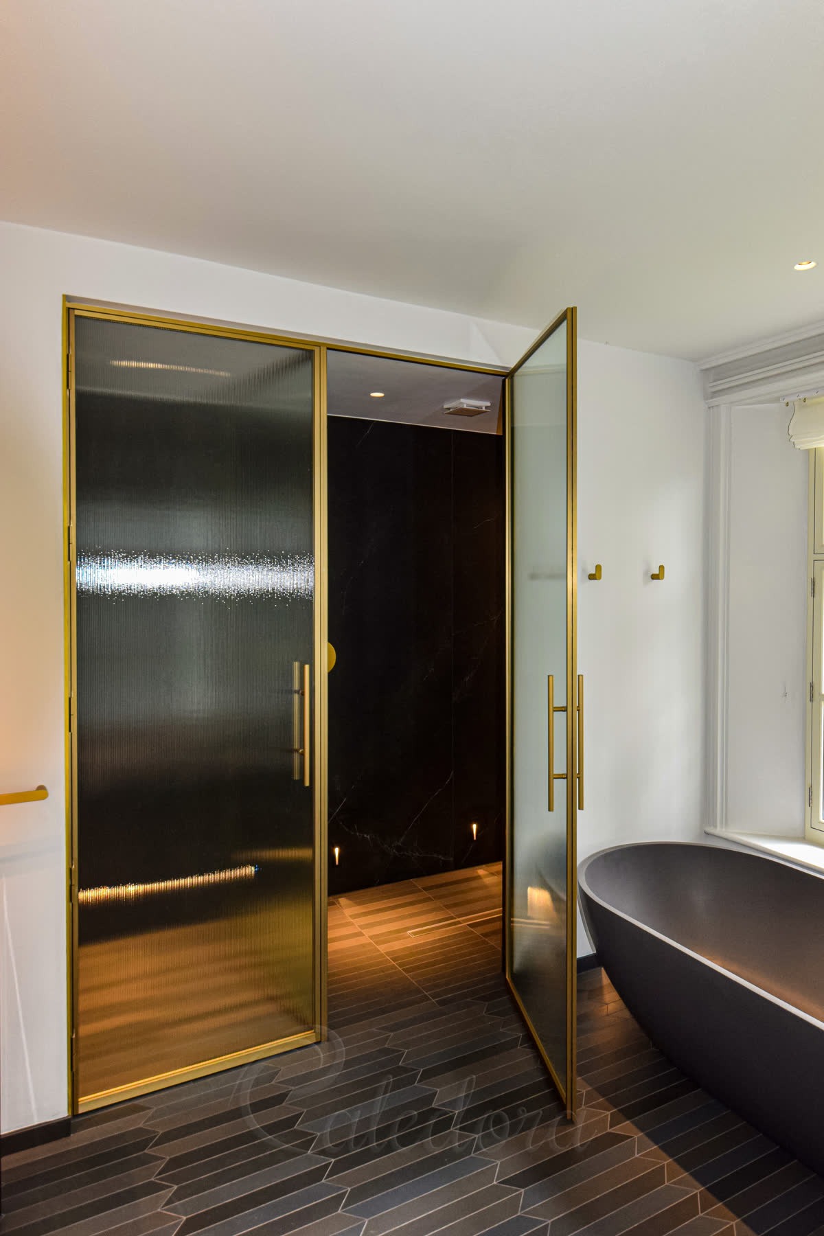 Open brushed brass shower door revealing the shower area with black marble tiles