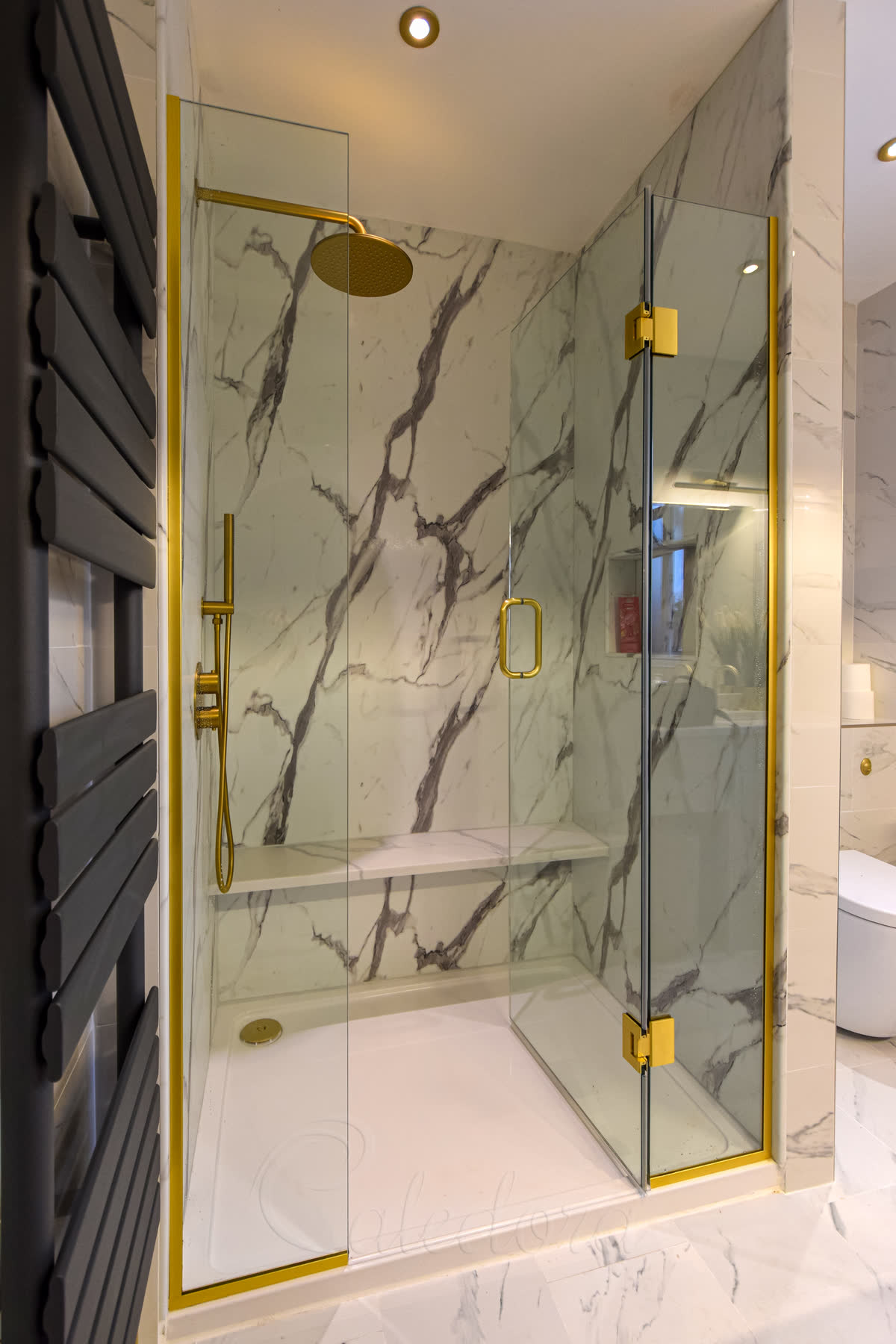Brushed brass shower screens with central door in marble-effect tiled bathroom