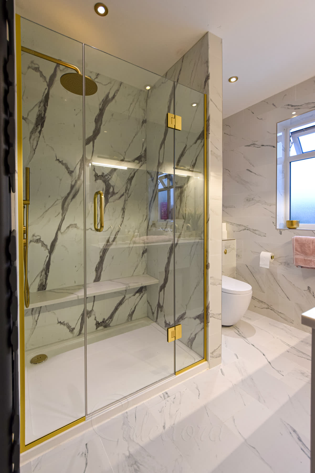 Brushed brass shower screens with central door in a marble-effect tiled bathroom