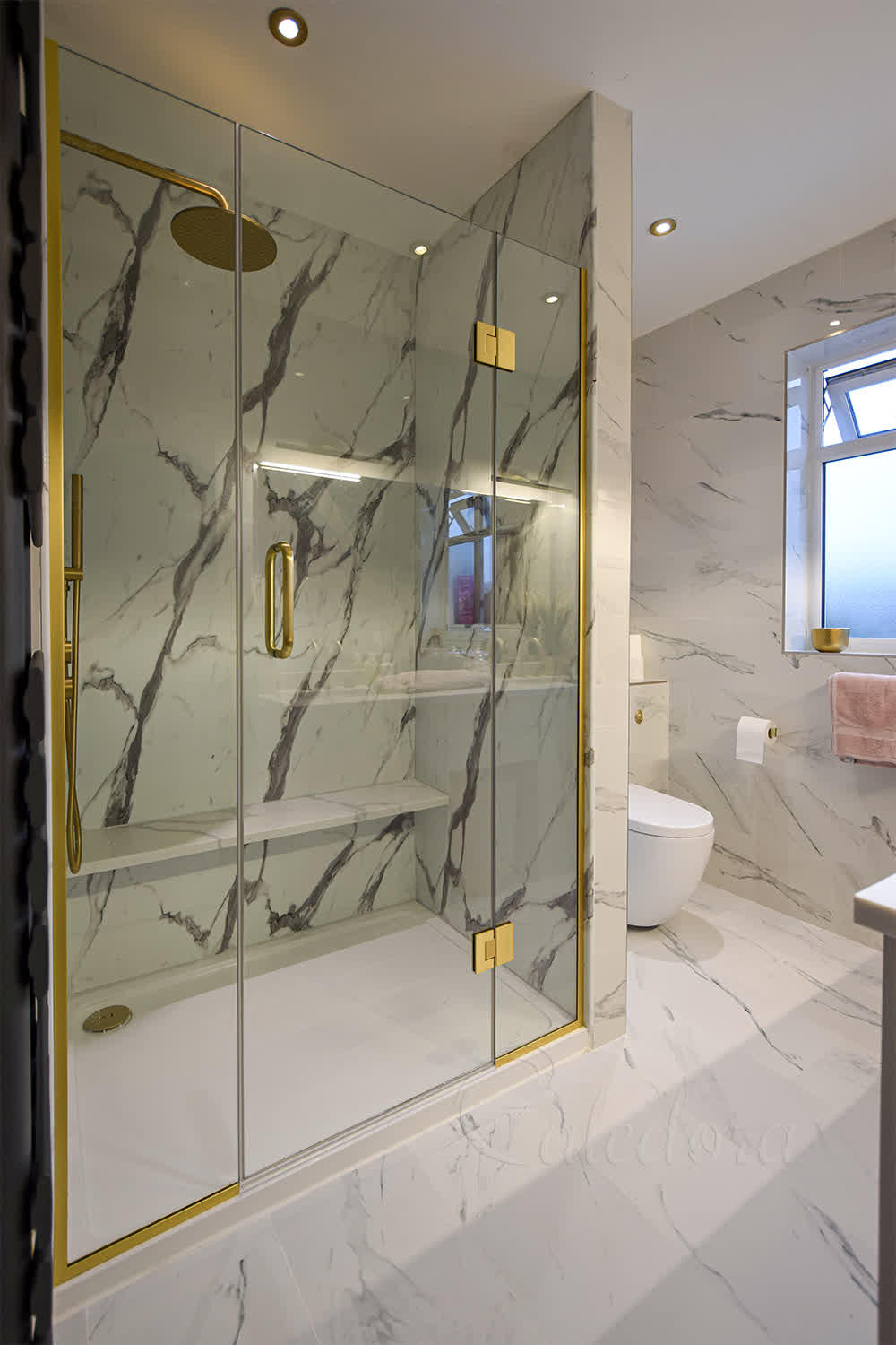 Brushed brass shower screens with central door in a marble-effect tiled bathroom
