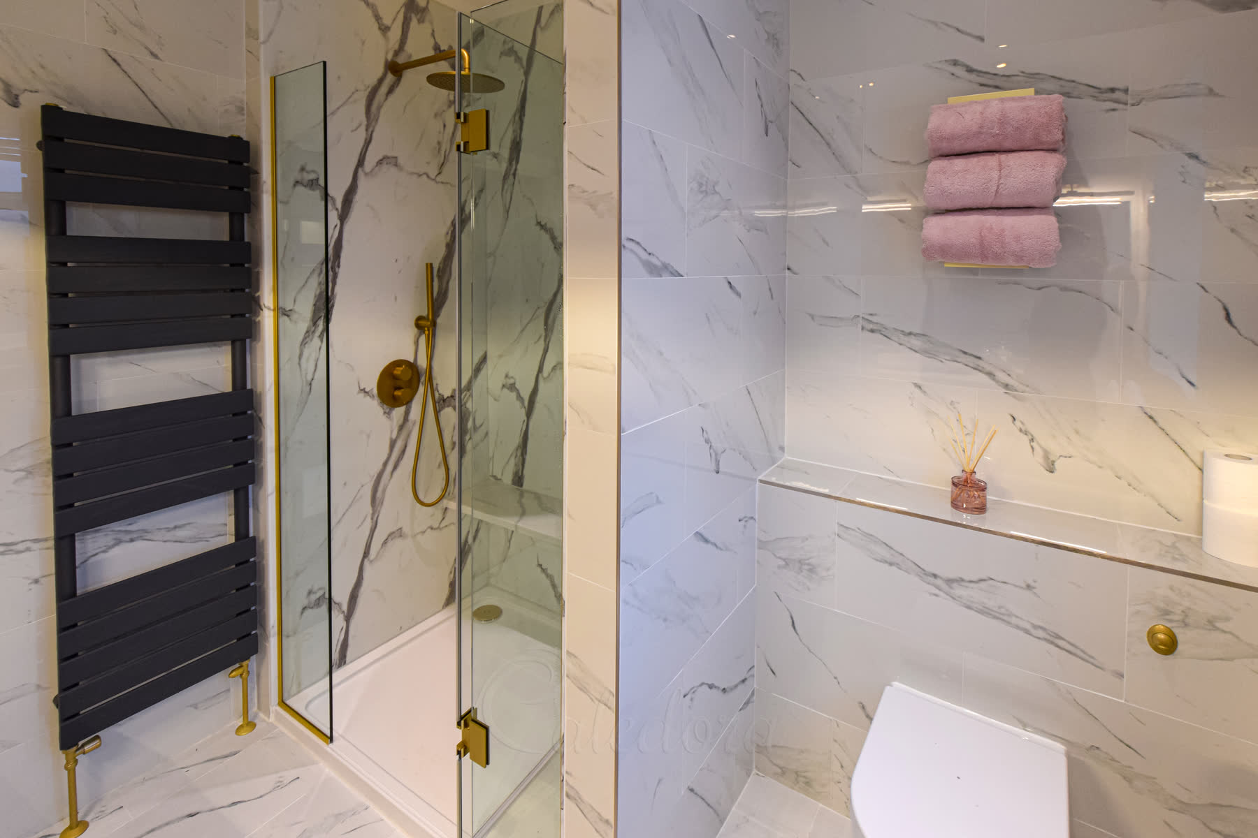 Wide view of brushed brass shower screen system with integrated door and black towel radiator