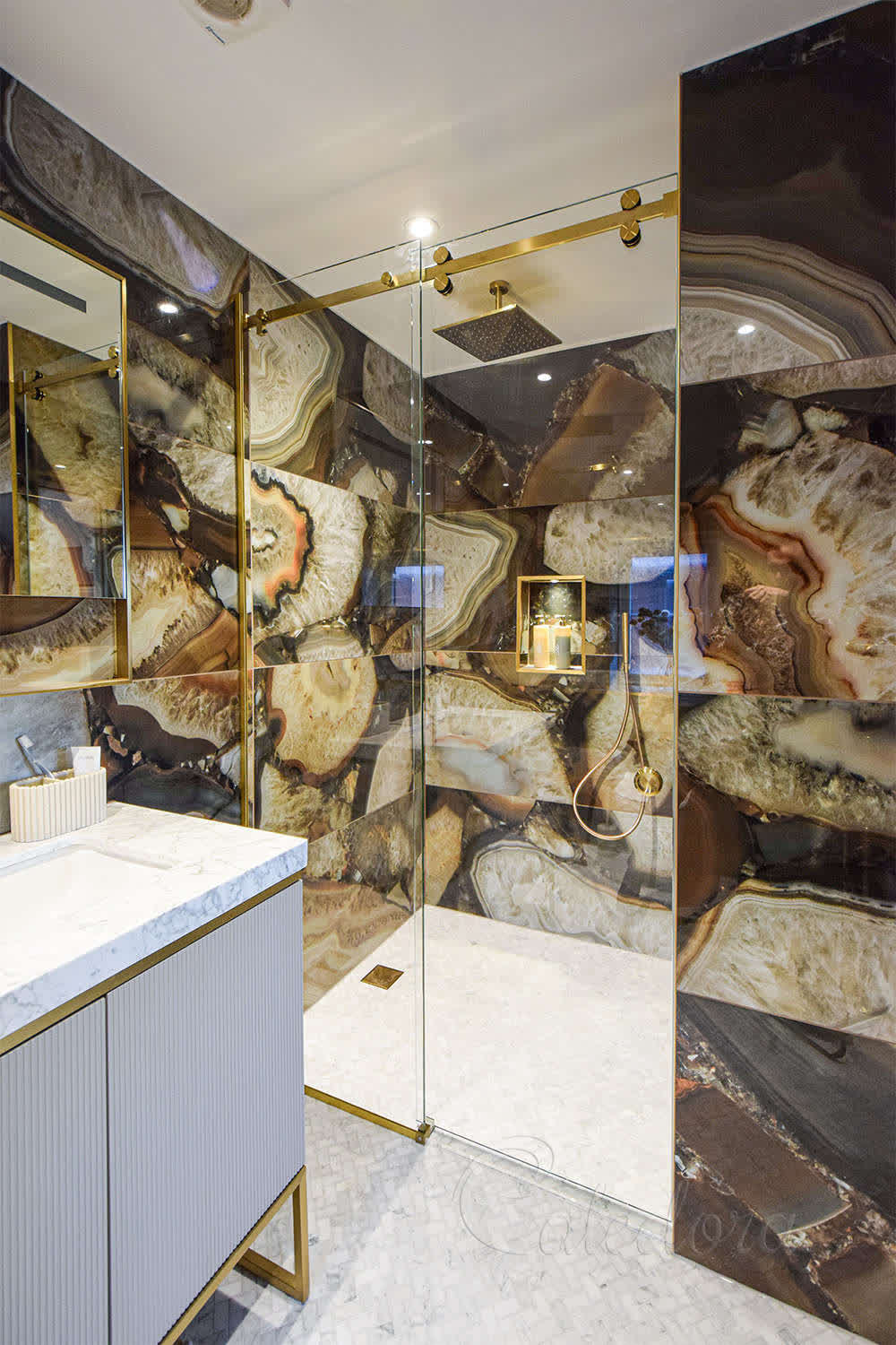Elegant brushed brass sliding shower door with ultra-clear glass in a luxury bathroom with marble walls