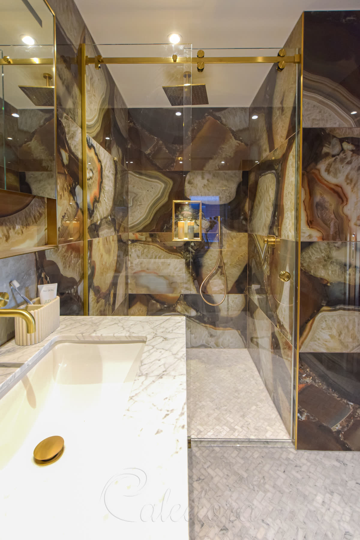 Close-up view of brushed brass sliding shower door with minimalistic seals and ultra-clear glass in a marble bathroom