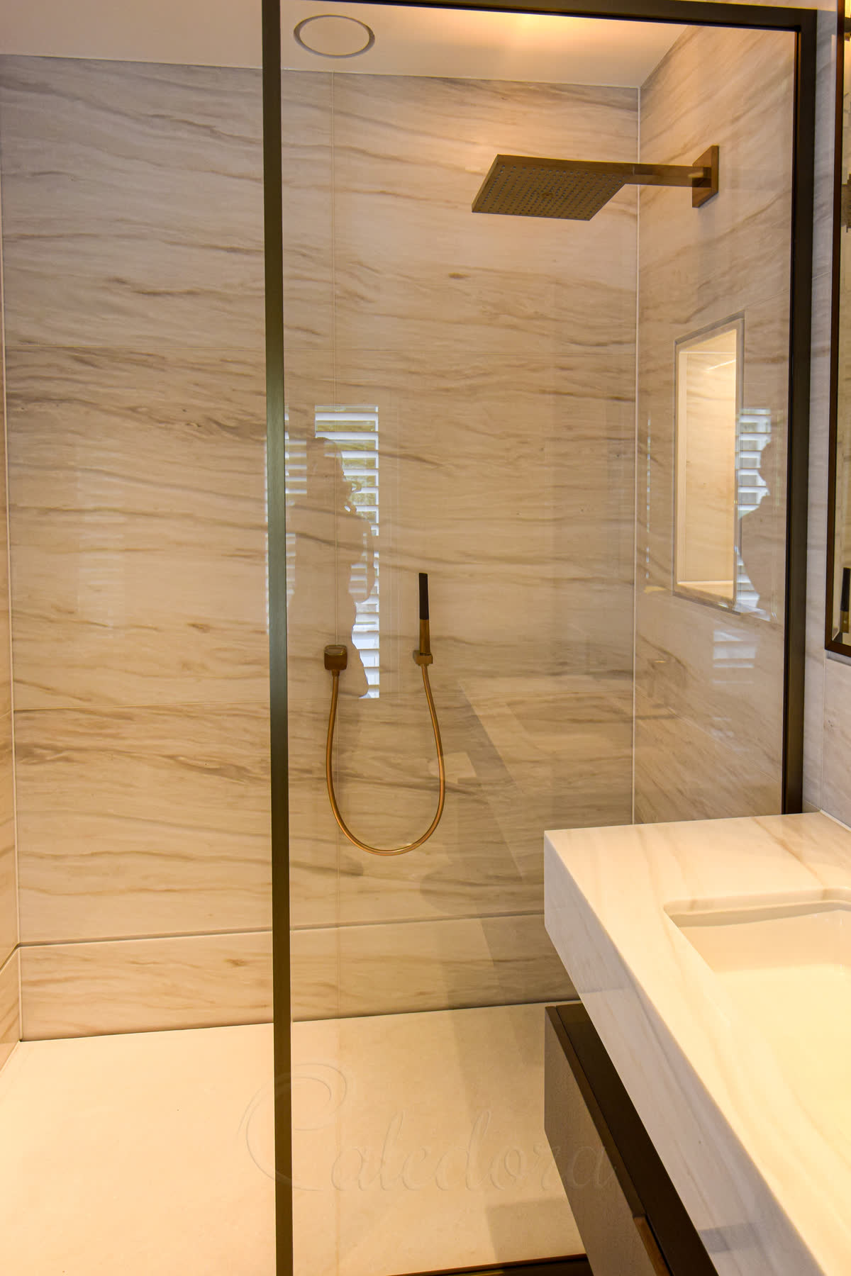 Close-up of brushed bronze frame shower screen showing the elegant textured finish against marble wall