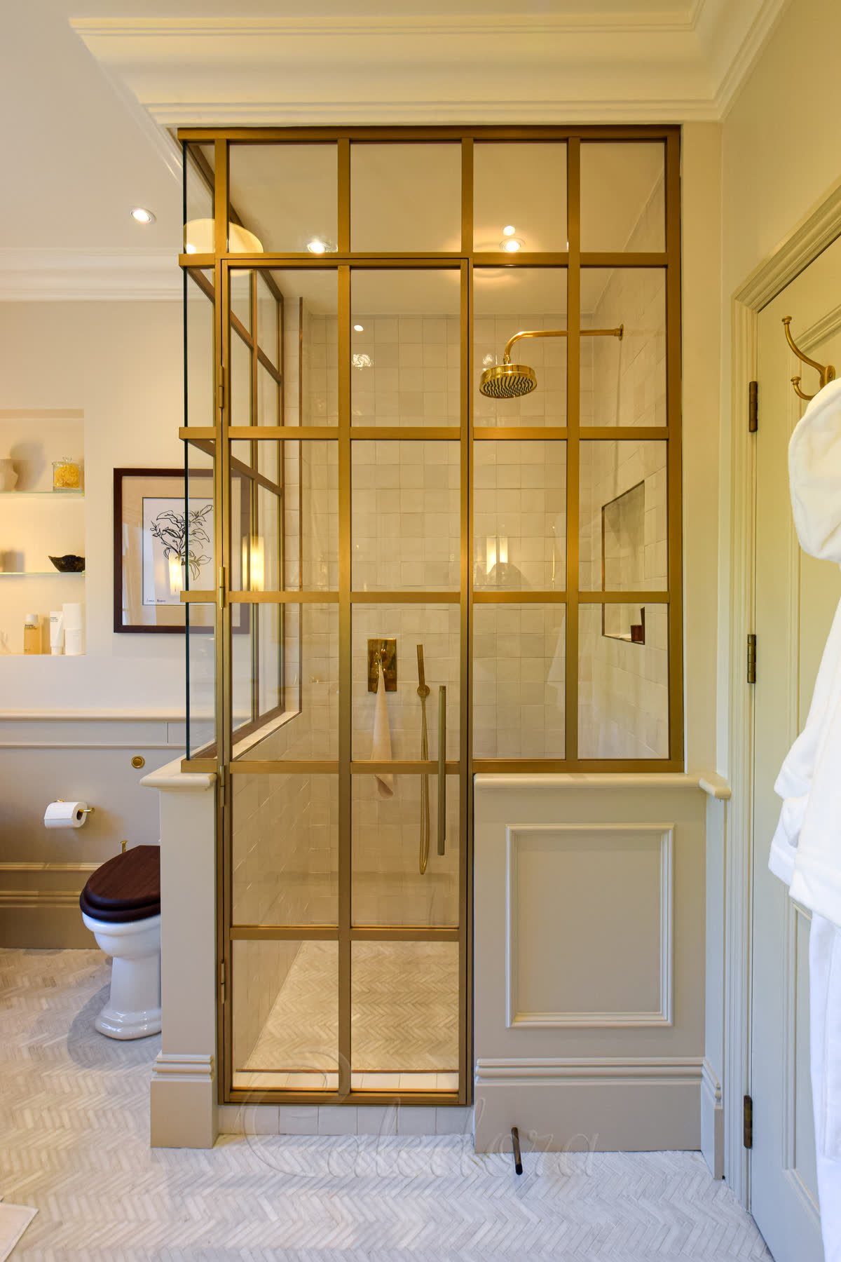 Corner shower enclosure with brushed gold frame and open door revealing ladder-style handle