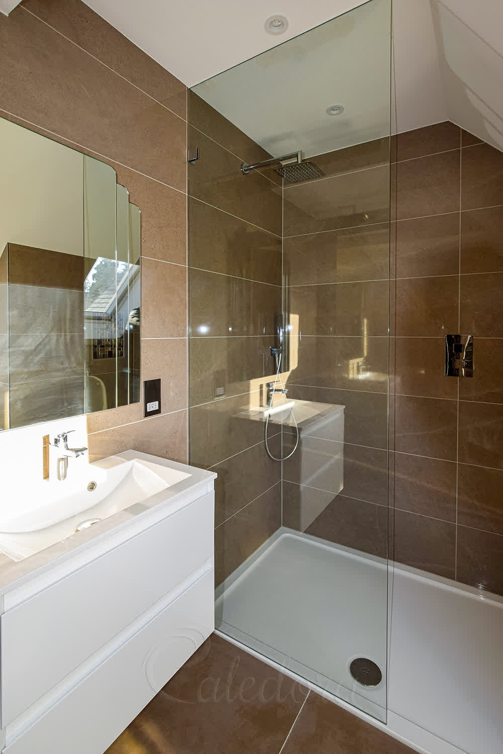 Full-height chrome shower screen with wall brackets in modern bathroom with brown tiles and white vanity