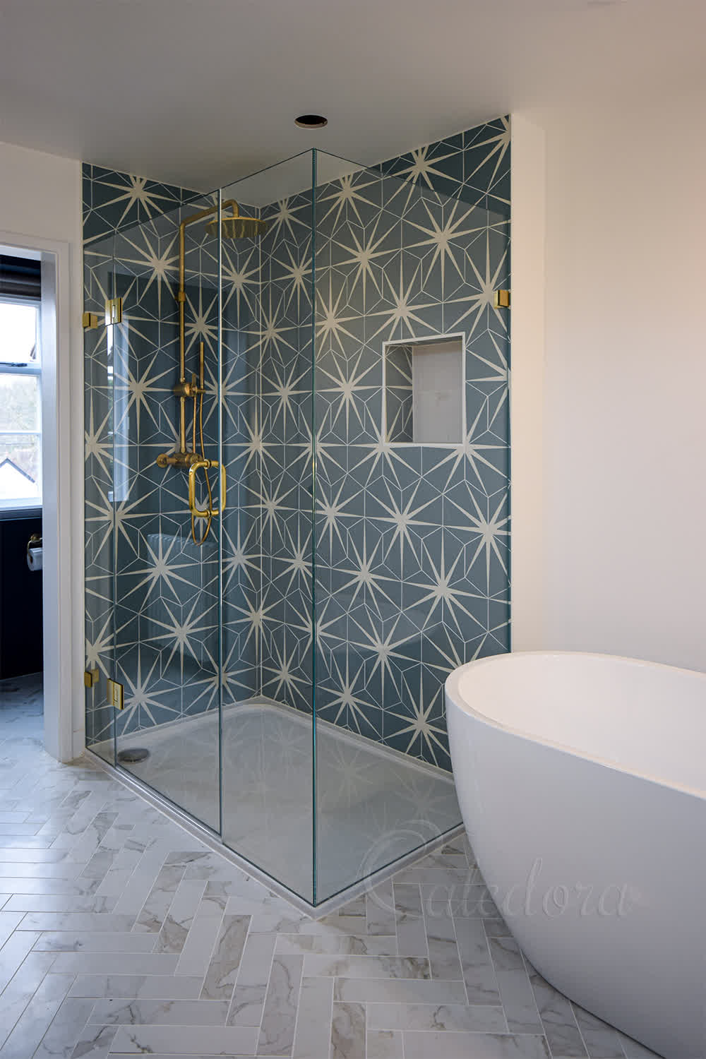 Frameless corner shower enclosure with blue patterned tiles and brushed brass fixtures