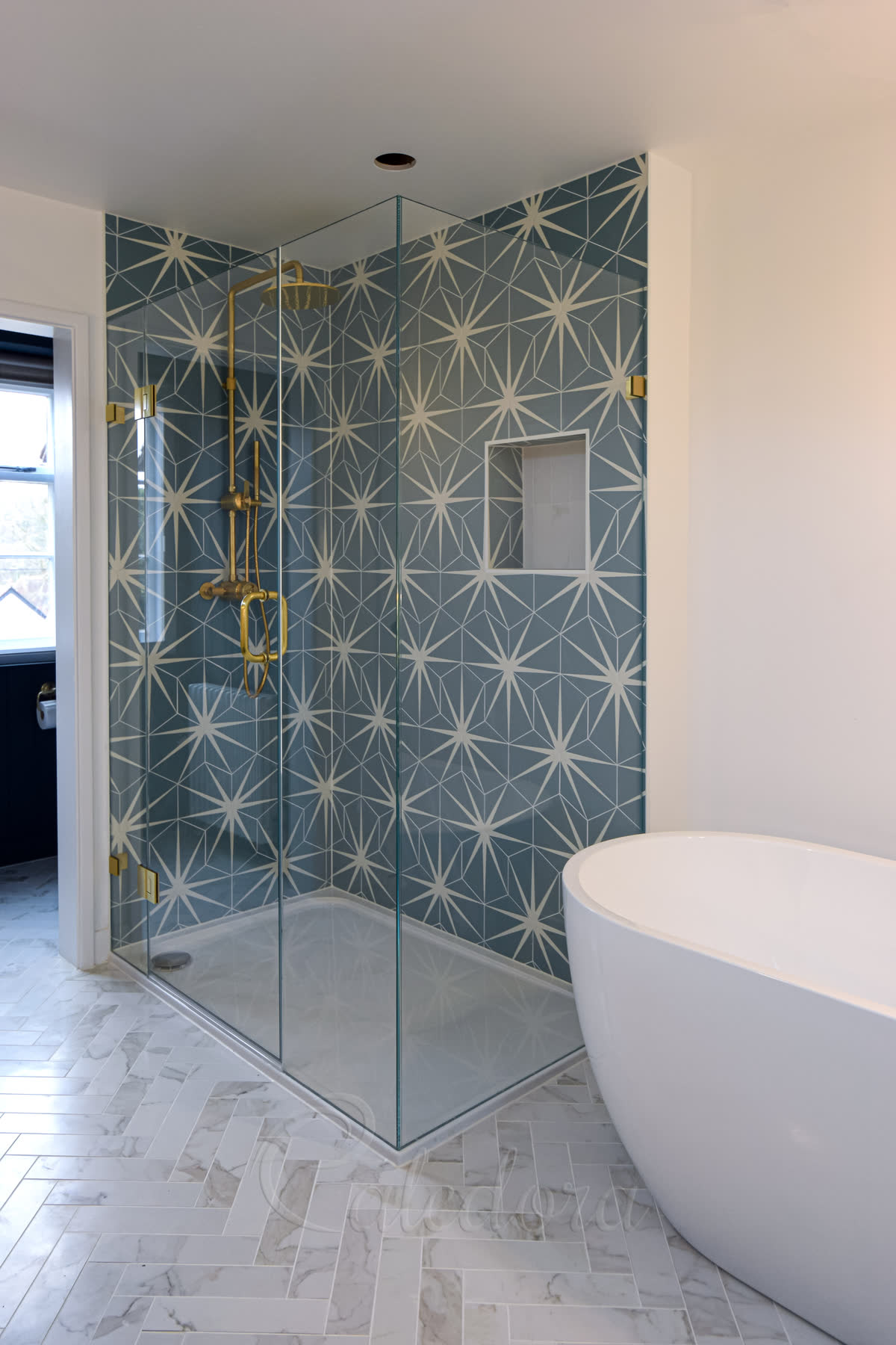 Frameless corner shower enclosure with blue patterned tiles and brushed brass fixtures