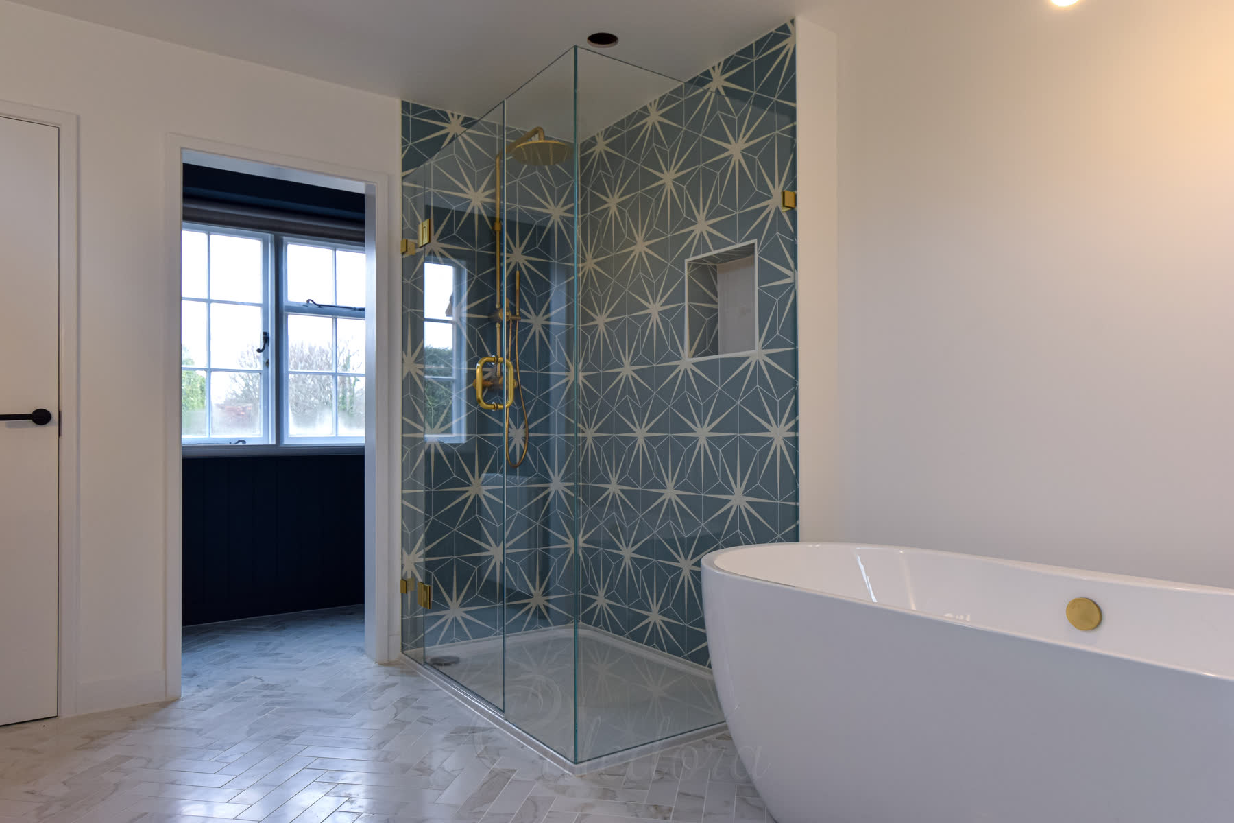 Wider view of bathroom with corner shower enclosure featuring blue geometric tiles and freestanding bathtub