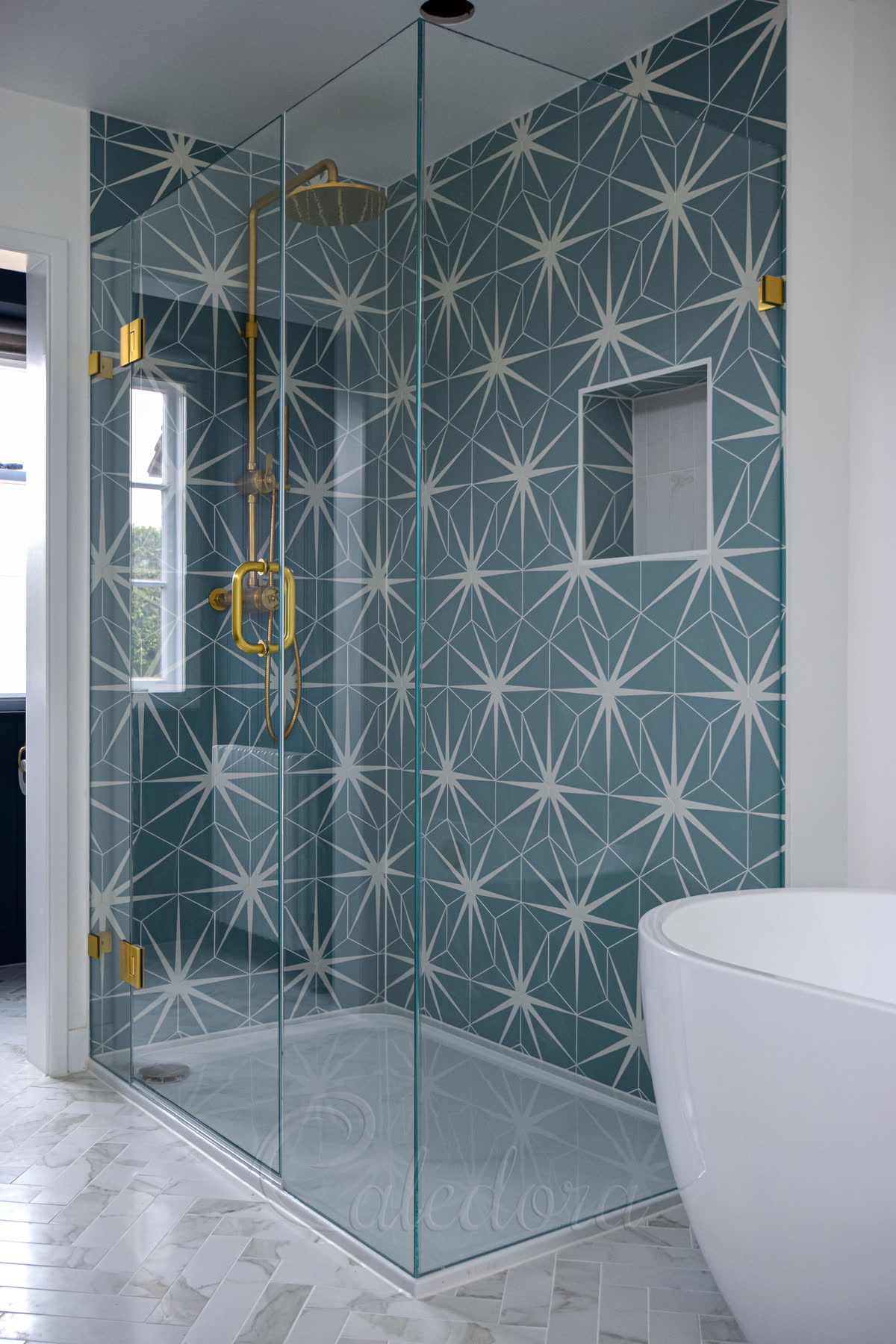 Close-up of corner shower enclosure with brushed brass hinges and handle against blue star pattern tiles