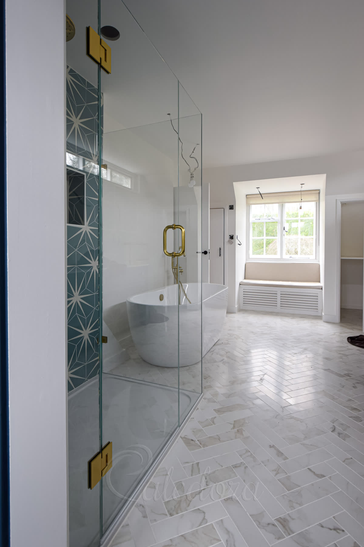 Side view of frameless glass shower enclosure showing the door mechanism and brushed brass hardware