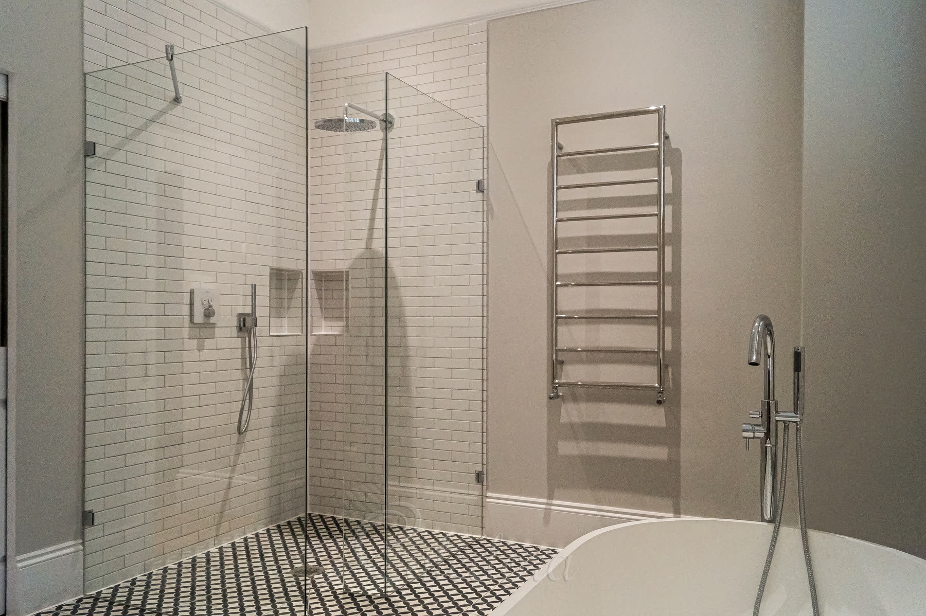 Walk-in shower area showing UV-bonded glass panels with chrome towel rail and black patterned floor tiles