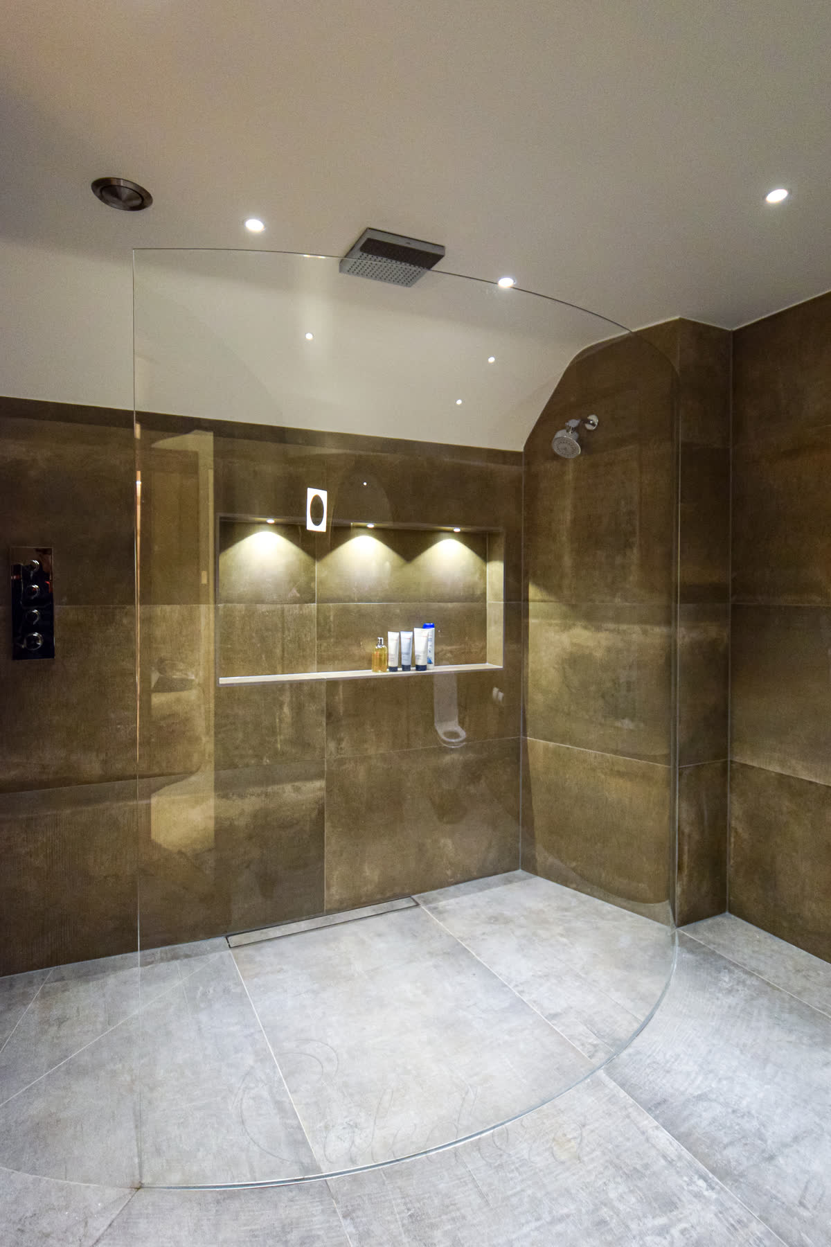 Frameless curved shower screen in luxury master bathroom with golden stone tiles