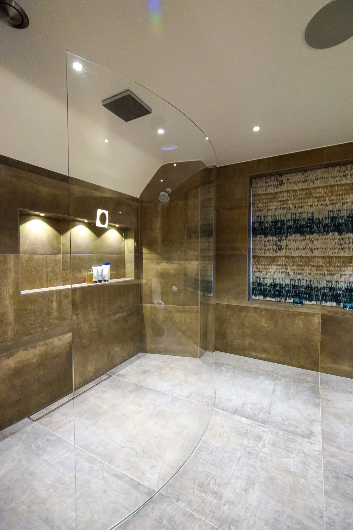 Curved glass shower screen with recessed wall fitting and golden stone bathroom tiles
