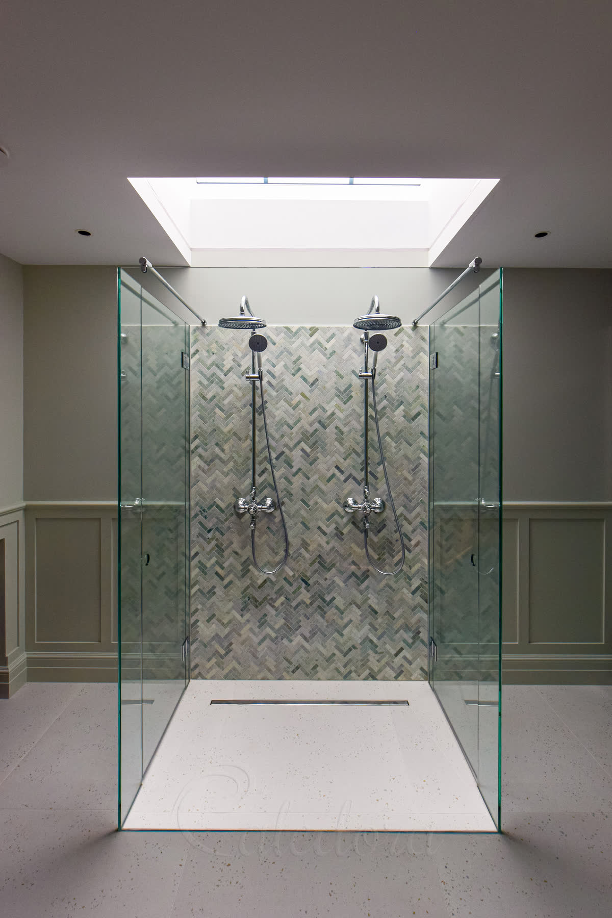 Inside view of double shower enclosure showing twin shower heads, herringbone tiles, and circular hole handles