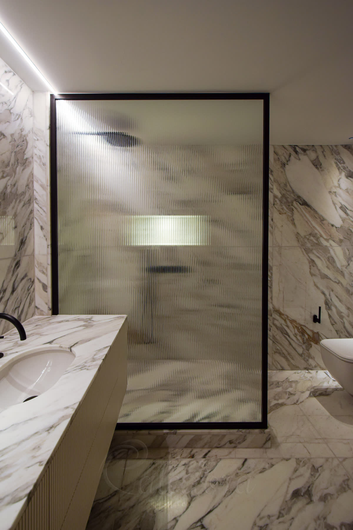 Fluted glass walk-in shower screen with black frame and reeded texture facing bathroom, installed in London
