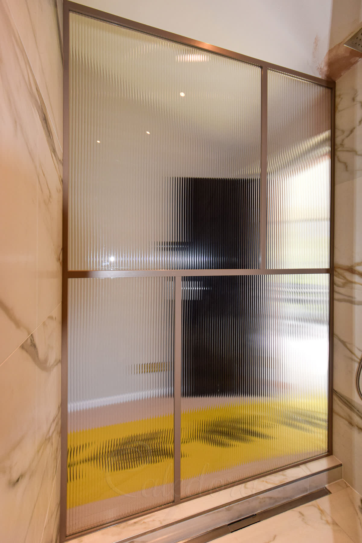 Bronze framed fluted shower screen with grid pattern viewed from bathroom side with marble walls