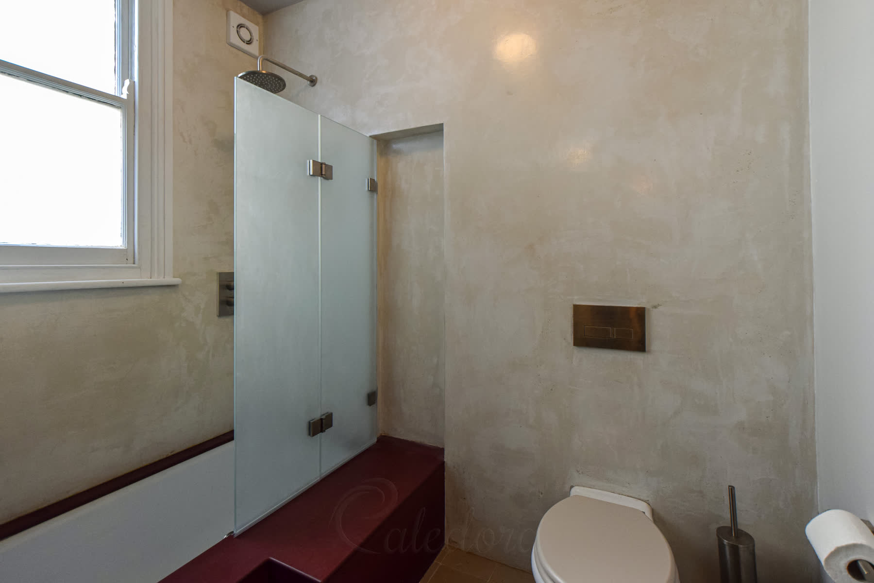 Wide view of the folding shower screen with the brushed nickel hinges and creamy microcement walls