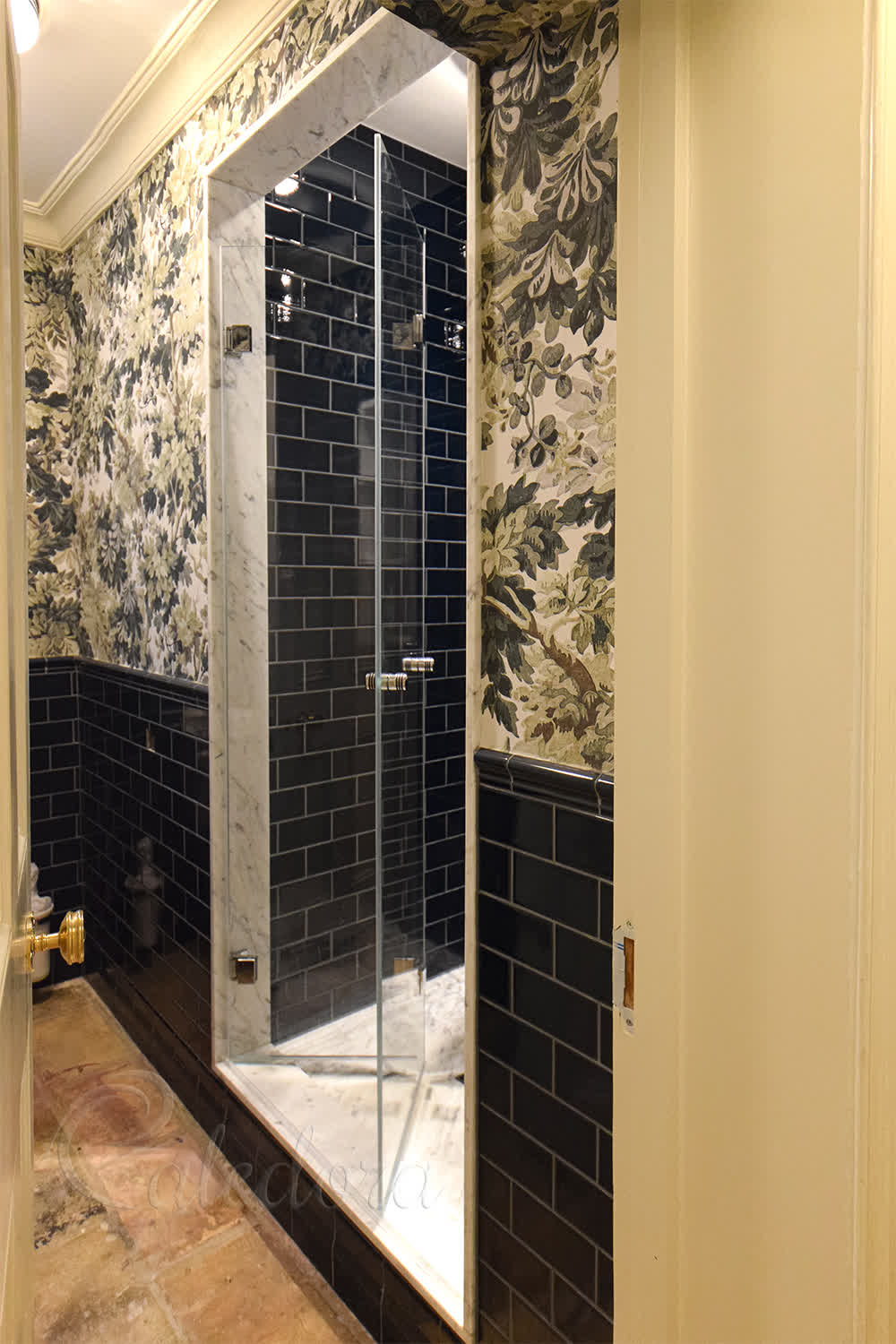 Frameless bifold shower door open showing black tiles and folding mechanism in Central London bathroom