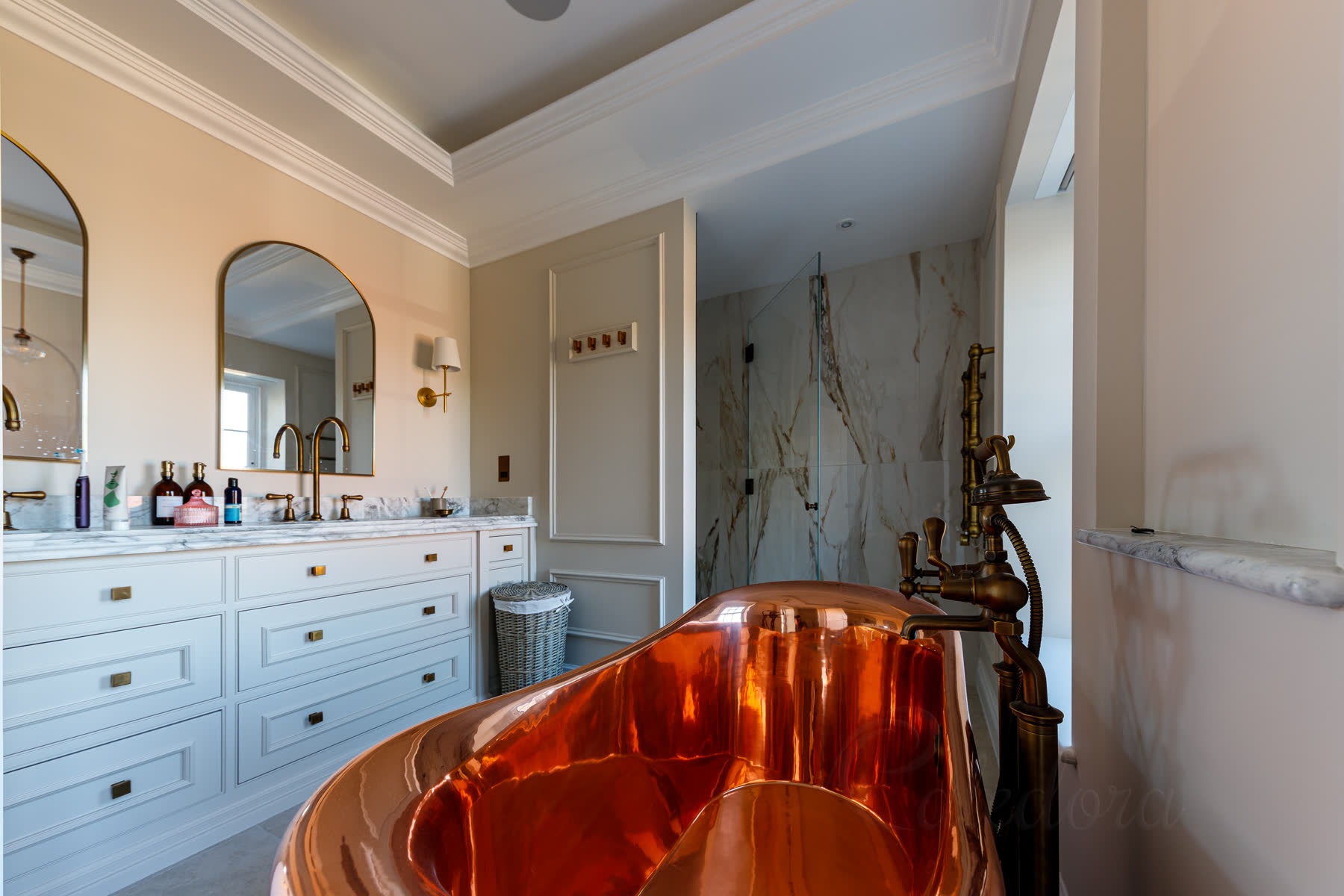 Antique brass frameless shower door in traditional bathroom with copper bath and marble-like tiling