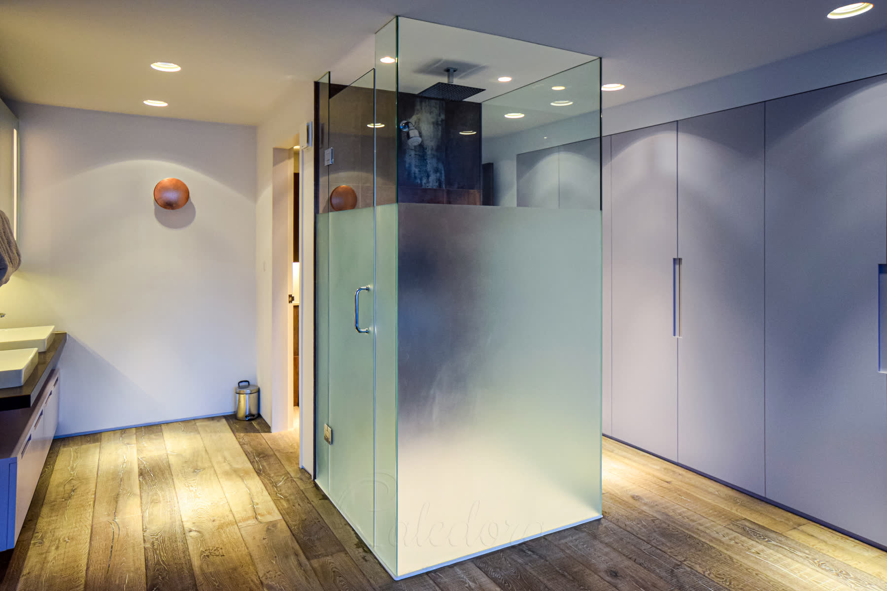 Full height frosted glass shower enclosure with ceiling-recessed panels on wooden floor