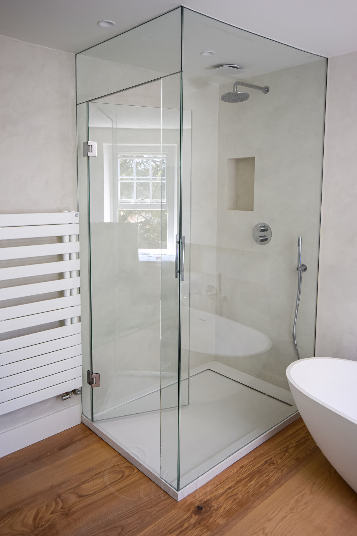 Floor to ceiling shower enclosure in corner bathroom with towel radiator and freestanding bath