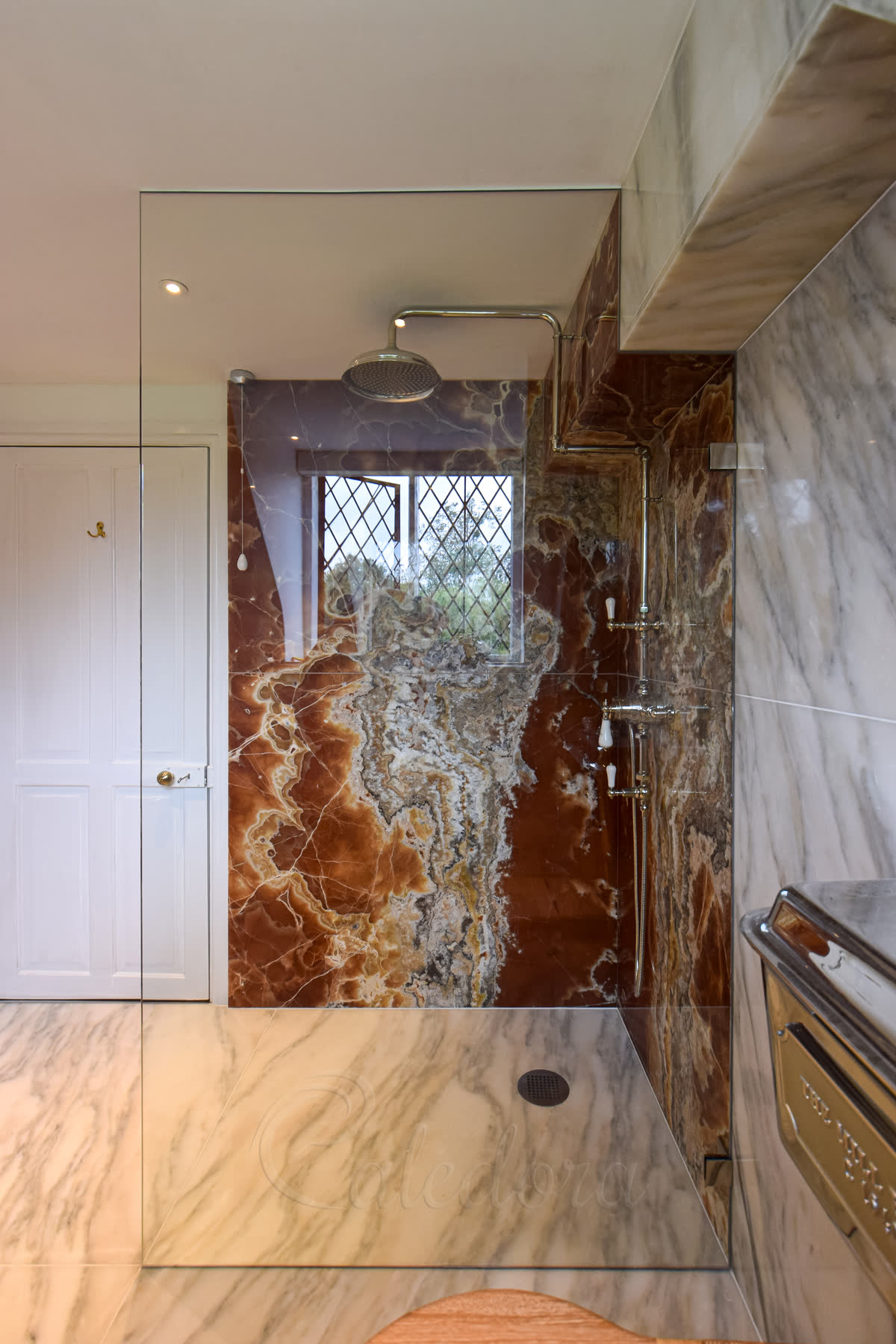 Polished chrome brackets securing full-height frameless shower screen in tiled bathroom