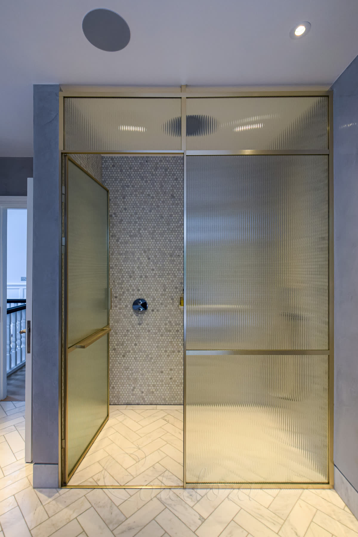 Open brass framed shower door showing mosaic tiled interior and level floor access