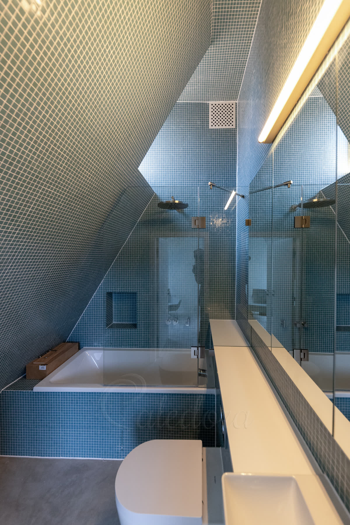 Frameless loft bath screen with brushed nickel hardware and CNC-cut notch around a corian-topped half-wall in a blue mosaic London bathroom