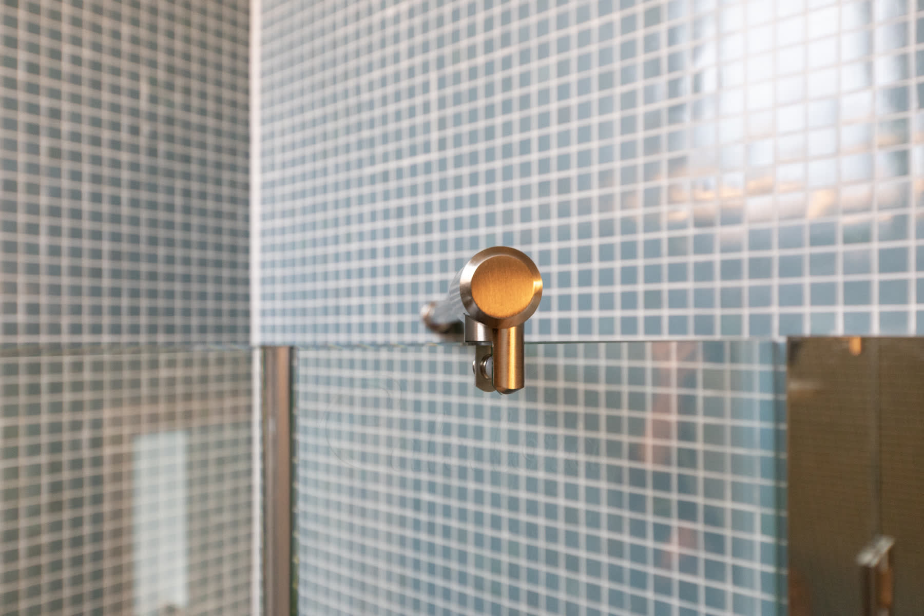 Close-up of the brushed nickel reinforcement bar bracket sitting on top of the fixed bath screen panel against blue mosaic tile