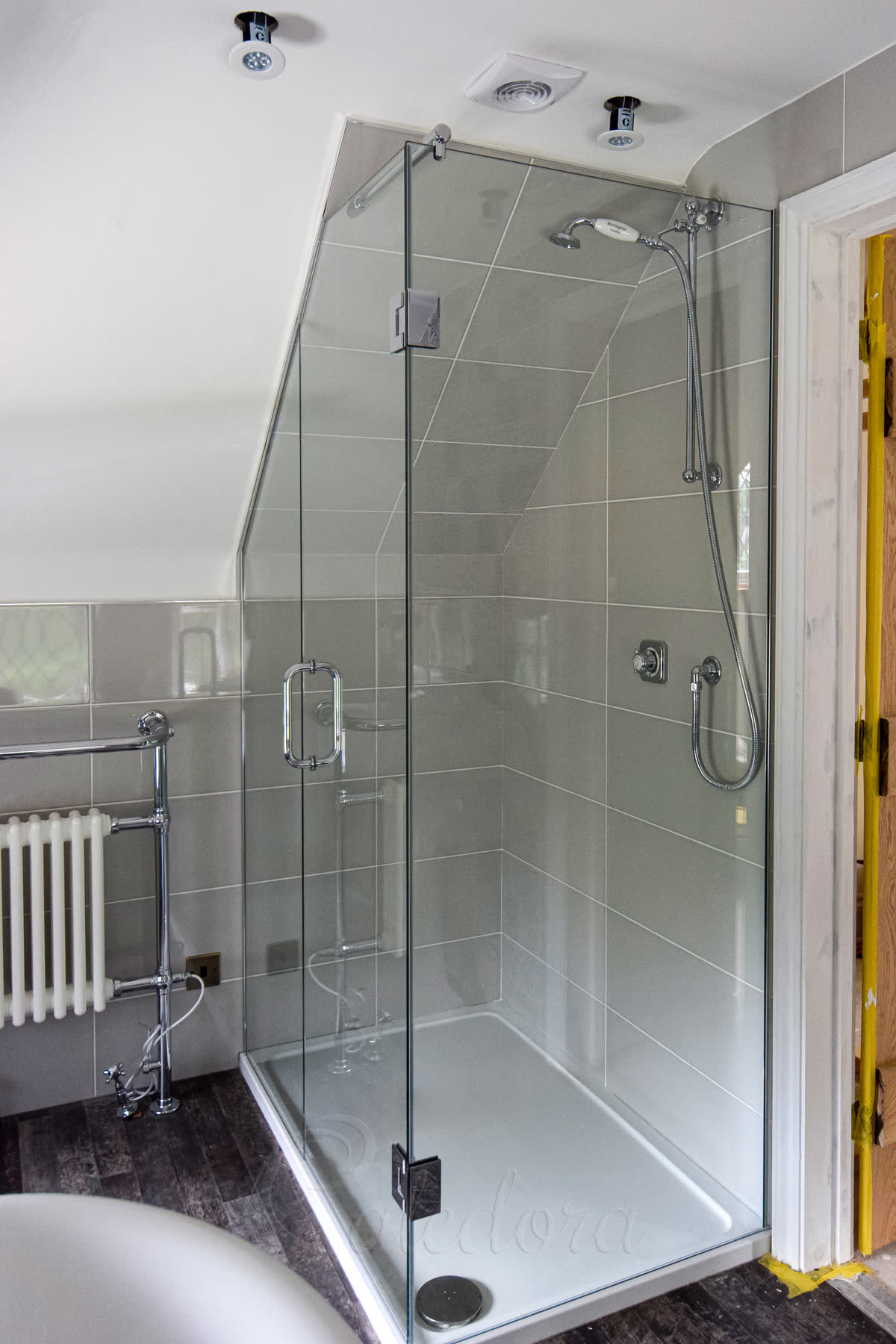 Corner loft shower enclosure installation with angled top following ceiling line and chrome wall brackets