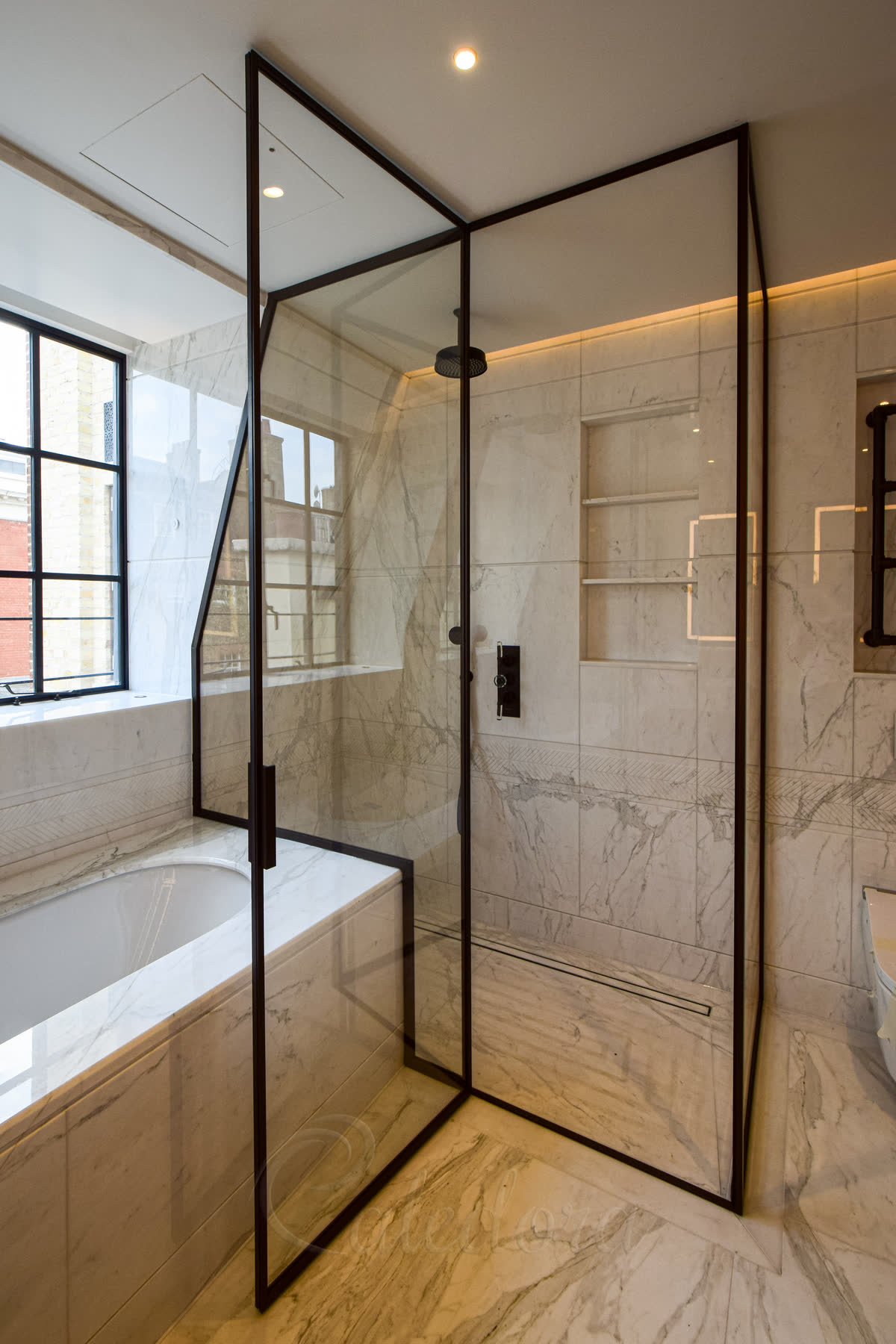 Luxury over bath shower enclosure with matching bronze hardware and marble walls