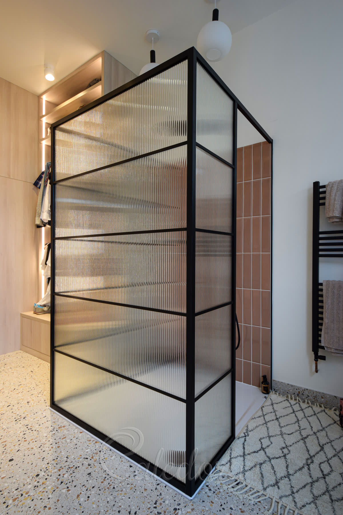 Corner view of walk-in shower enclosure with black grid frame and reeded glass