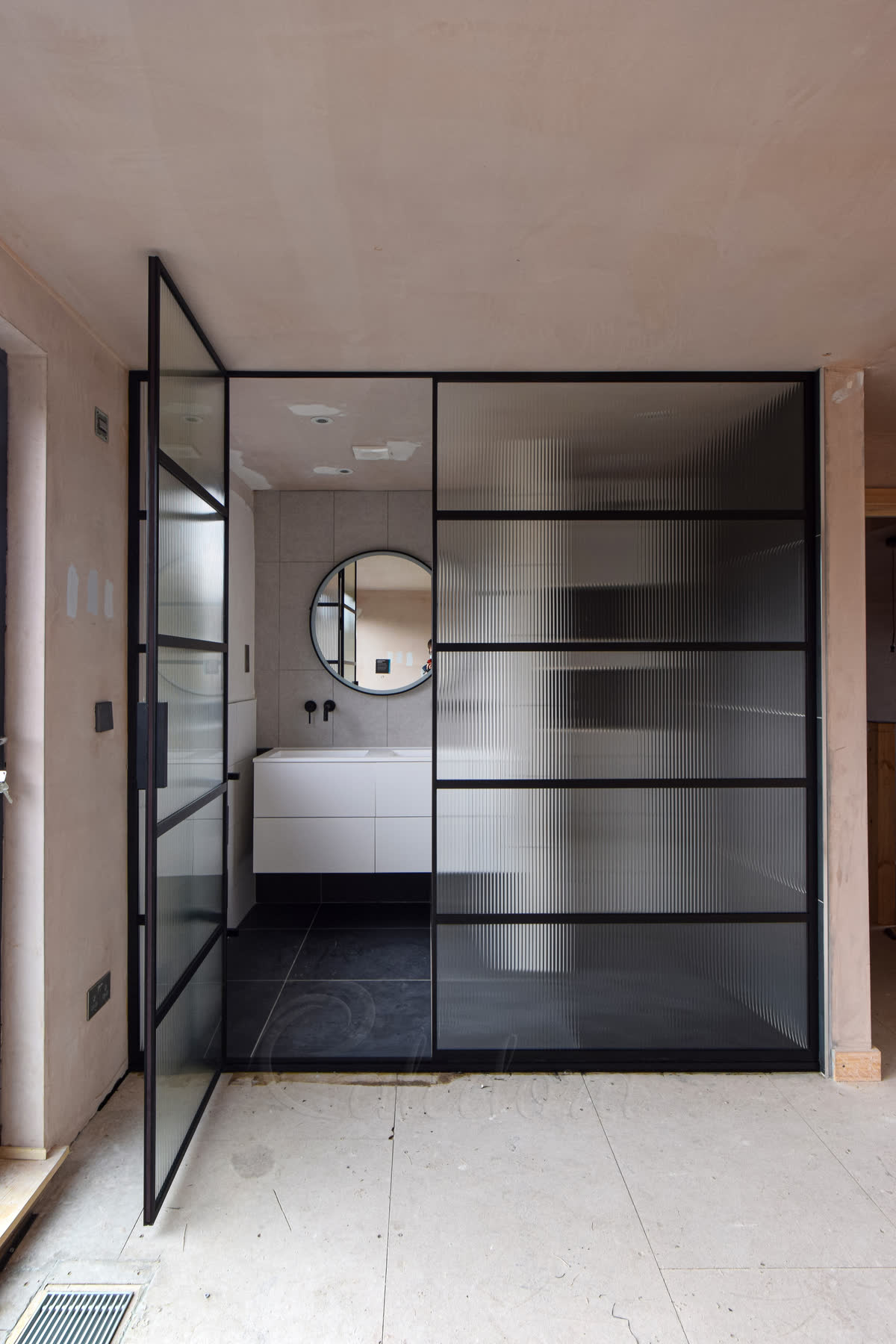 Ribbed glass shower screen with black frame and open swing door showing modern London bathroom with white vanity