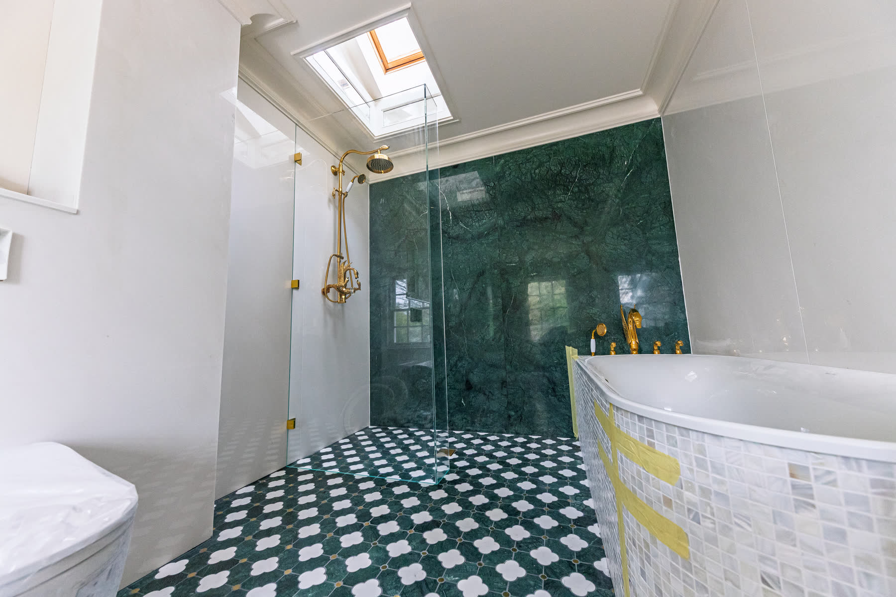 Walk-in shower screen with return panel in bathroom with green marble walls and geometric patterned floor