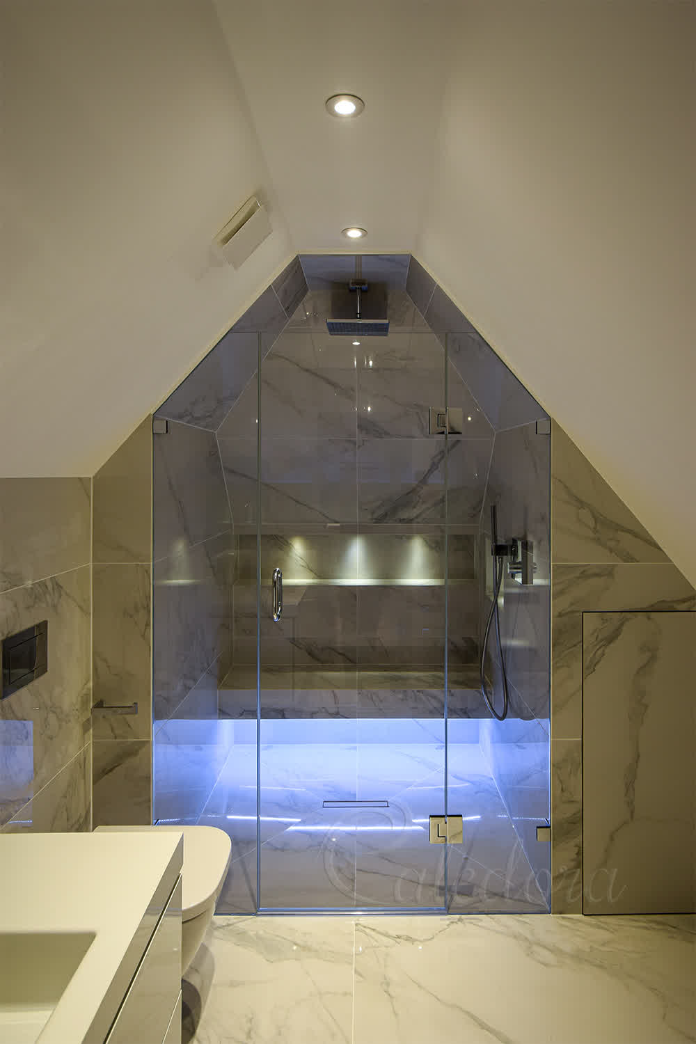 Frameless shower enclosure with glass-to-glass hinges under vaulted ceiling in tiled London bathroom