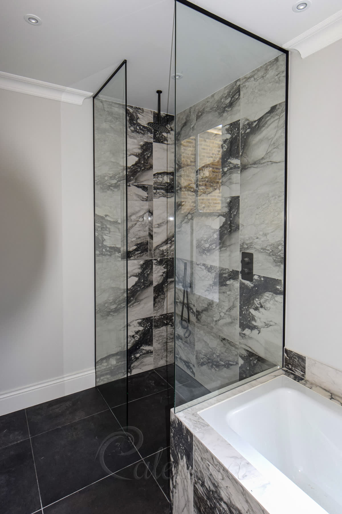 Black-framed frameless shower screens installed at bath level and floor level with black marble tiles