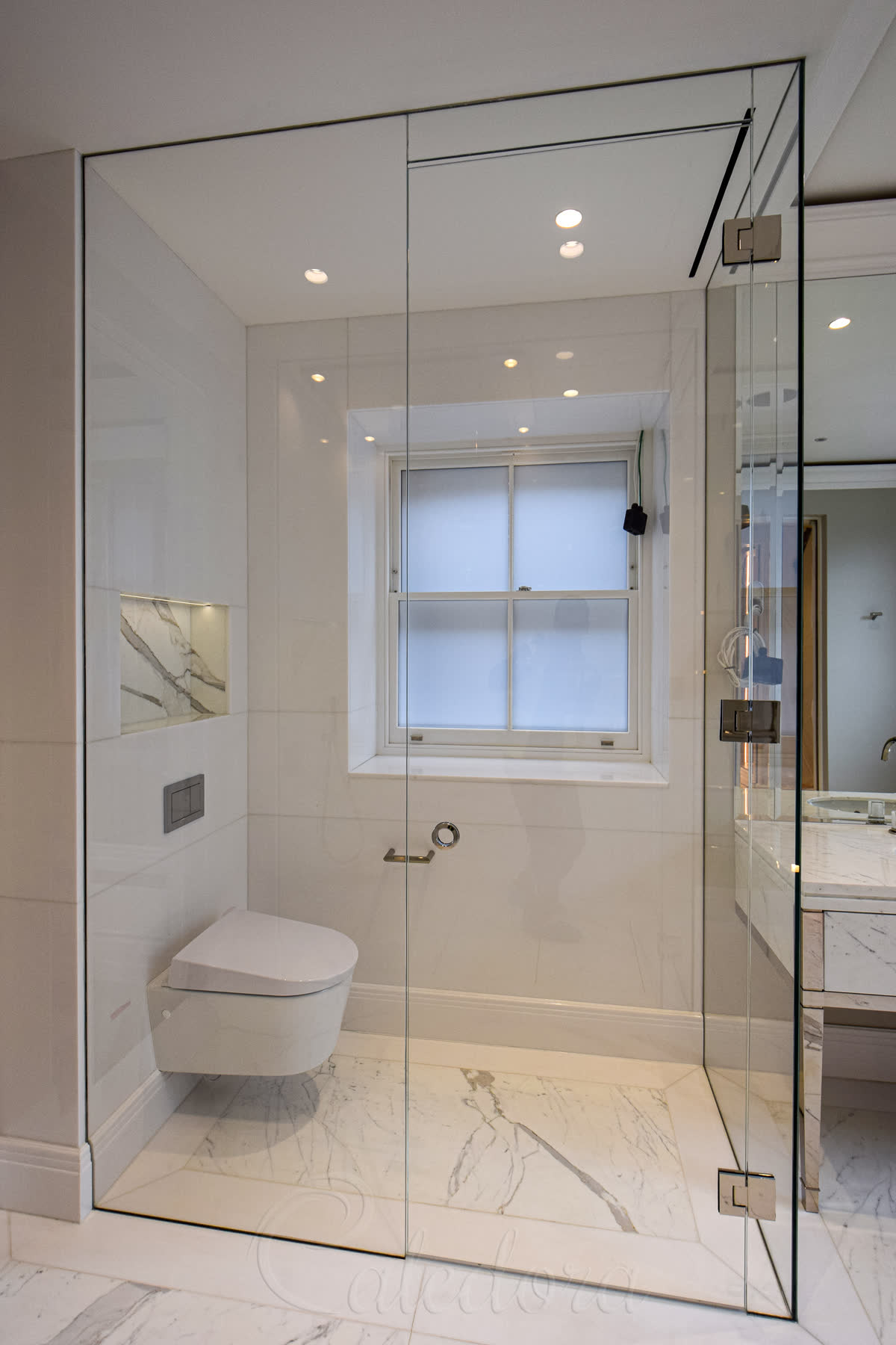 Matching glass enclosure for WC with walk-in floor design in corner of London luxury bathroom