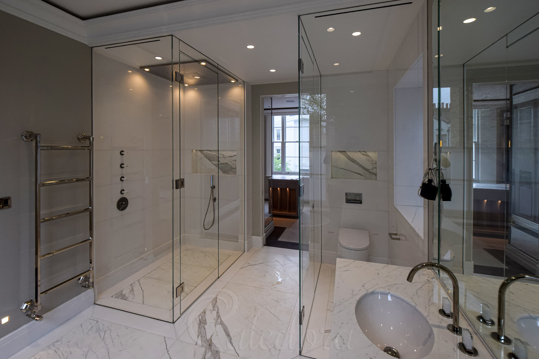 Overall view of two matching wet room shower enclosures with level marble floors in the London luxury bathroom