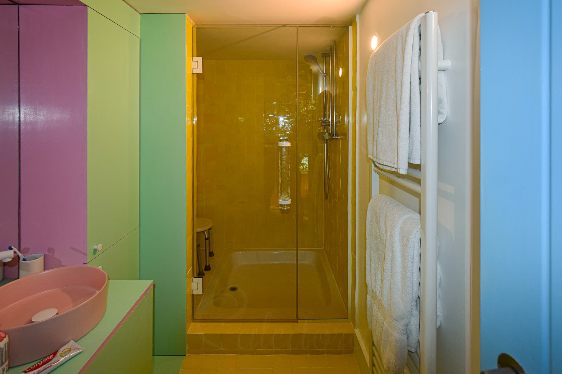 White hinged shower door bathroom overview showing colourful yellow, pink and green tiles