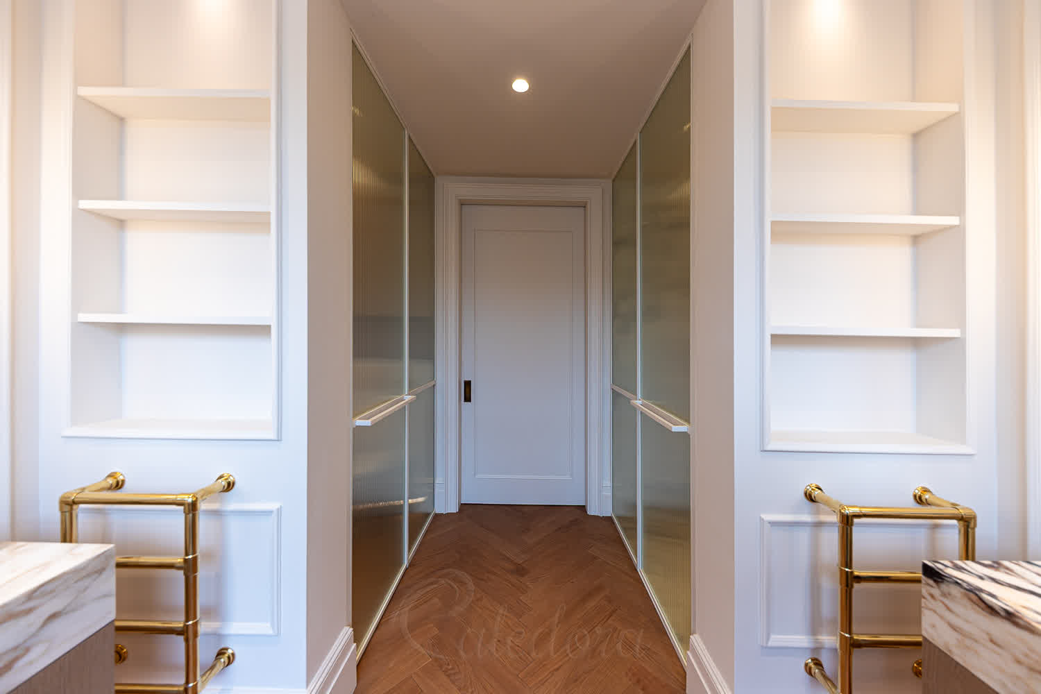 White framed fluted glass corridor between two matching shower partitions with brass towel warmers