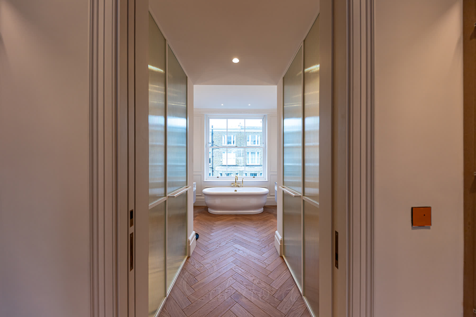 Walkway view between white framed glass partitions leading to bathroom with freestanding bath