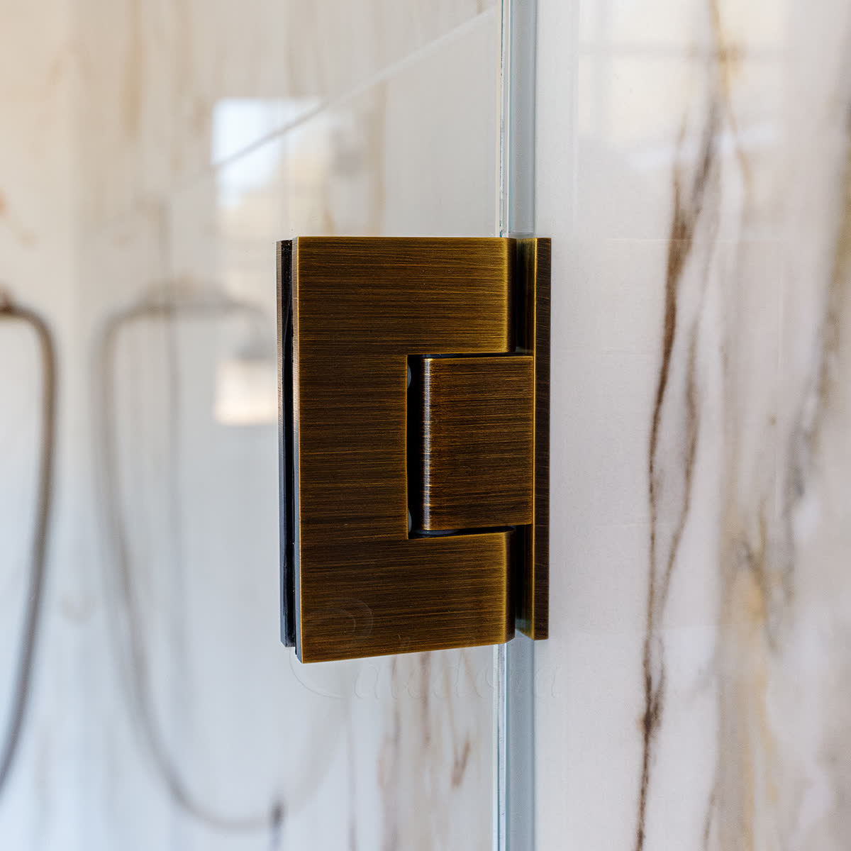 Close-up of an antique brass frameless hinge against a Calacatta marble wall — 8mm PVC perimeter seal visible as a thin strip along the glass edge above and below the hinge body, demonstrating Caledora's minimalist installation with no clip-on hardware